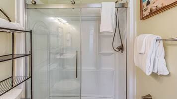 A glass-enclosed shower stall with a towel rack and a metal shelf unit beside it.