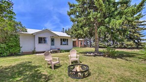 Une maison avec un jardin devant, deux chaises Adirondack et un foyer extérieur.