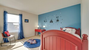 A bedroom with a red bed, a blue wall with Disney characters, a window with blue curtains, and a small desk with a lamp. - Backyard Oasis & Games: Davenport Magic Stay! (Davenport)