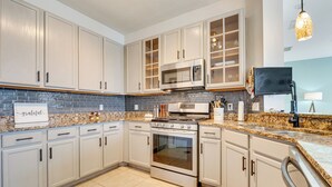 A modern kitchen with white cabinets, a granite countertop, stainless steel appliances, and a backsplash. - Backyard Oasis & Games: Davenport Magic Stay! (Davenport)