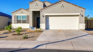 A two-story house with a garage, a small front yard with landscaping, and a clear blue sky. - Private Pool: Relaxing Phoenix Area Vacation Home! (Buckeye)