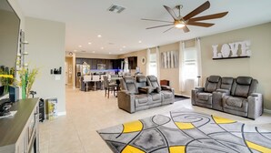 A modern living room with a gray sofa, a dining area, and a kitchen in the background. - Private Pool: Relaxing Phoenix Area Vacation Home! (Buckeye)