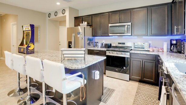 A modern kitchen with dark cabinets, stainless steel appliances, and a bar area with white stools. - Private Pool: Relaxing Phoenix Area Vacation Home! (Buckeye)