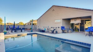 A swimming pool with blue-tiled edges, outdoor seating, and a building with a beige exterior. - Private Pool: Relaxing Phoenix Area Vacation Home! (Buckeye)