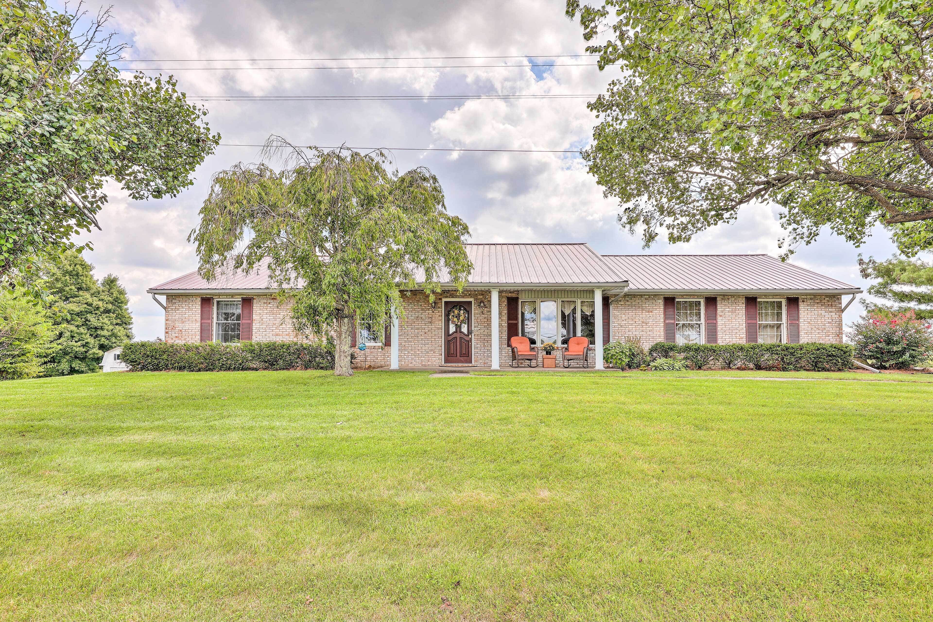 A two-story brick house with a front porch, a lawn, and trees.