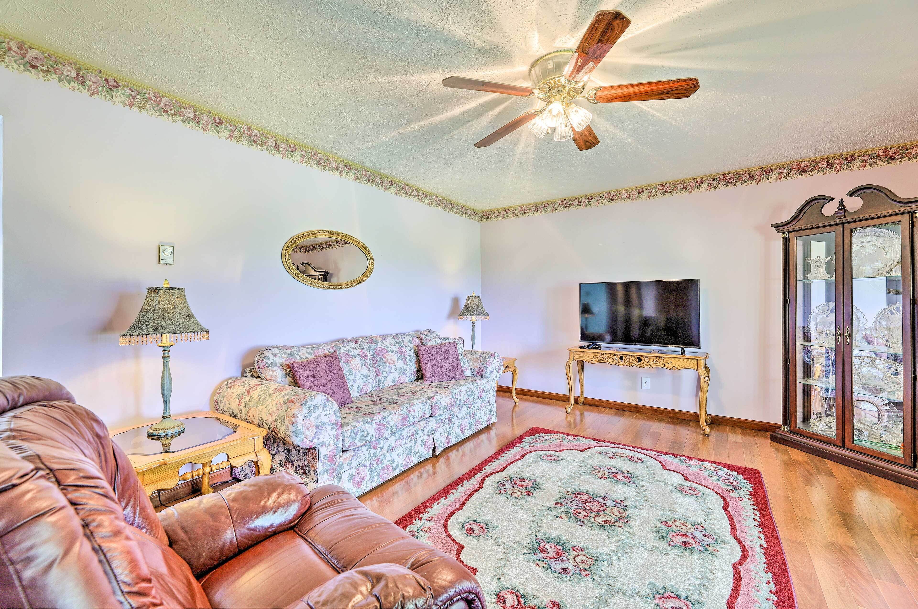 Un salon comprenant un canapé, un divan en cuir, un téléviseur, un ventilateur de plafond et un meuble avec des portes en verre.