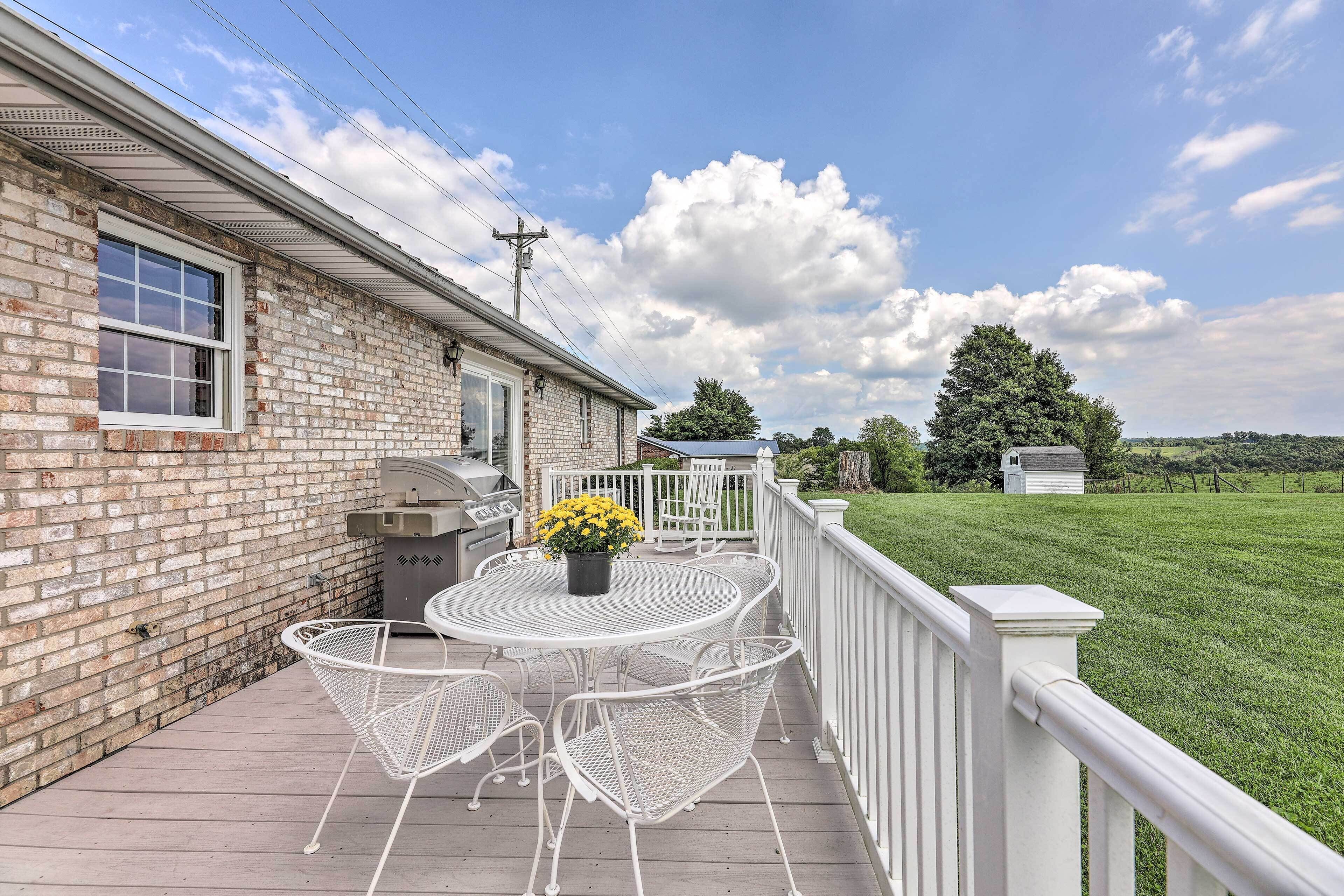 A patio with a round table and white metal chairs, a grill, and a flower pot.