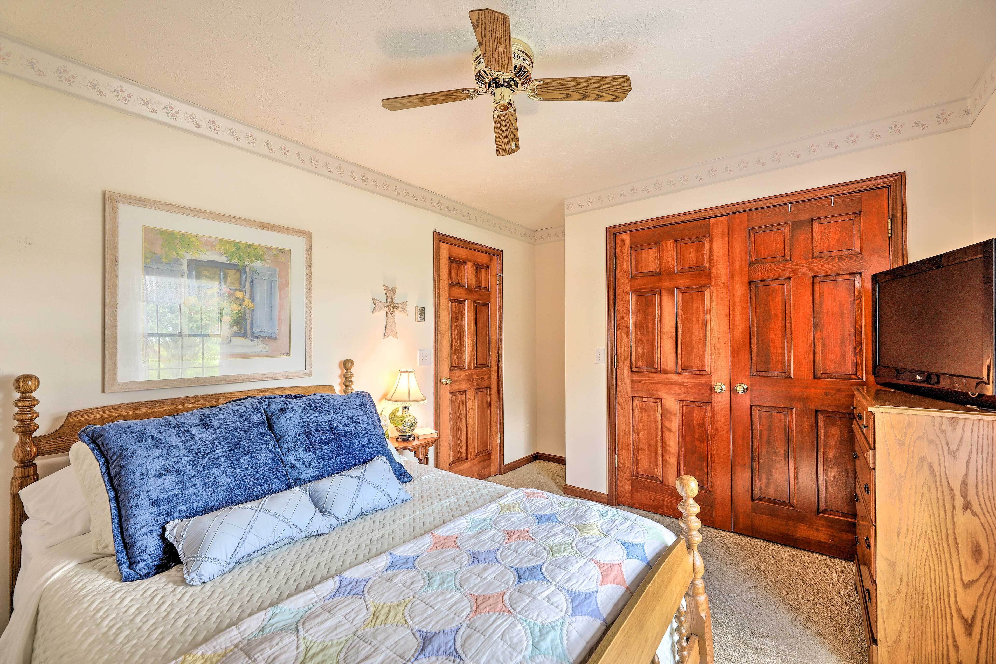 A bedroom with a bed, wooden wardrobe, a ceiling fan, and a television.