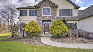 A two-story house with a stone facade, a central entrance with a red door, and two symmetrical trees in the front yard.