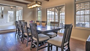 A dining area with a wooden table and chairs, large windows, and a hanging light fixture.