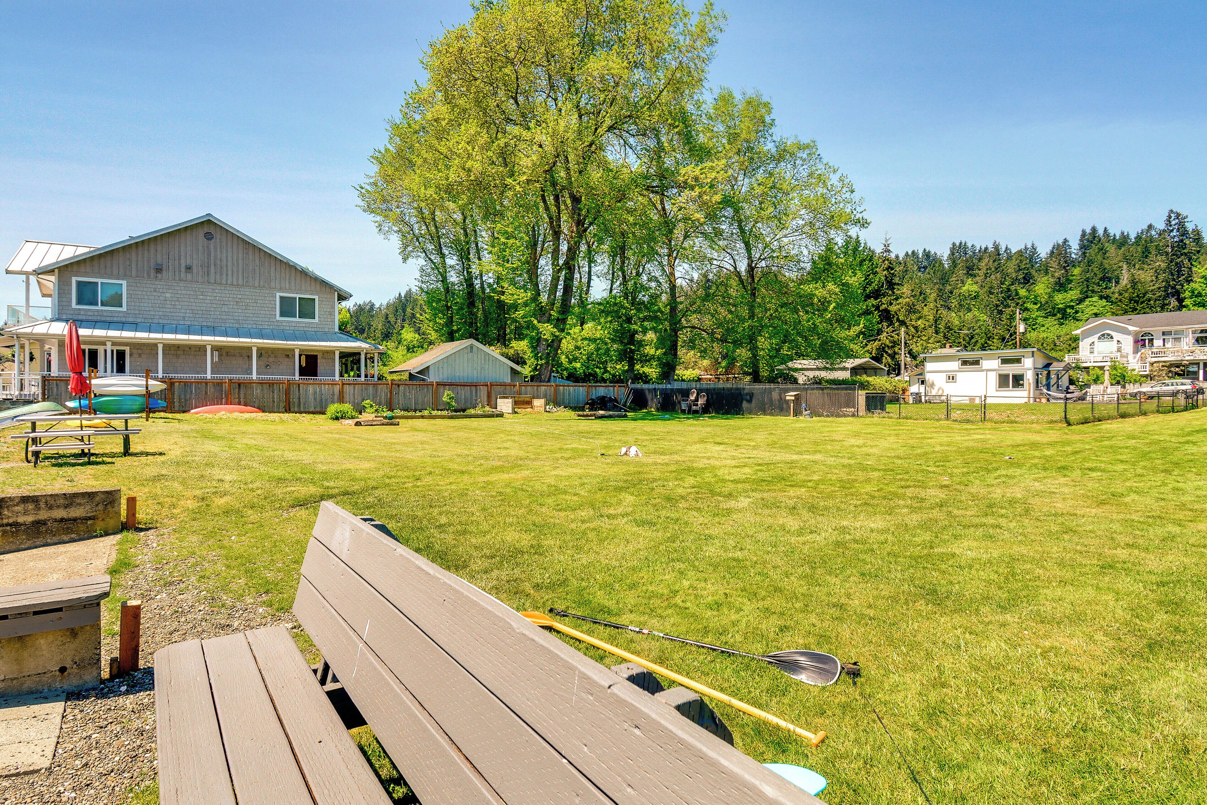 A grassy backyard with a wooden bench, picnic table, and fishing rods.