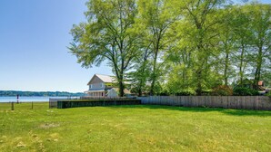 A grassy area with a wooden fence, a house, and a body of water in the background. - Waterfront Hood Canal Cottage: Steps to the Beach! (Belfair)
