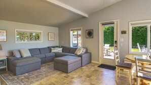 A living room with a grey sectional sofa, a rug, and a dining area with wooden chairs and a table. - Waterfront Hood Canal Cottage: Steps to the Beach! (Belfair)