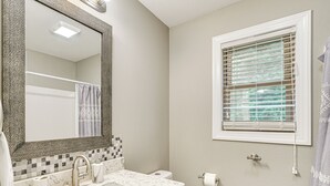 Een badkamer met een wastafel, spiegel, toilet en raam met zonwering.