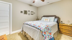 Een slaapkamer met een bed, een plafondventilator, een nachtkastje en aan de muur bevestigde fotolijstjes.