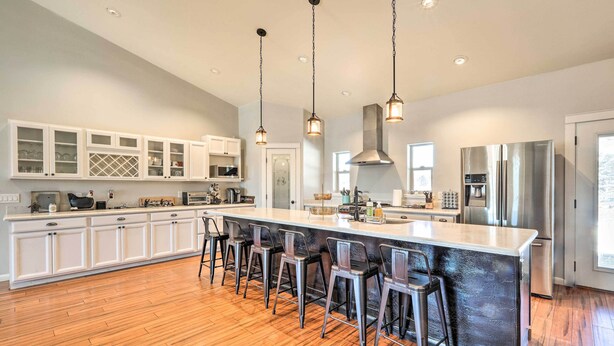 Una cocina moderna con una isla grande, taburetes de bar, muebles blancos, electrodomésticos de acero inoxidable e iluminación colgante.