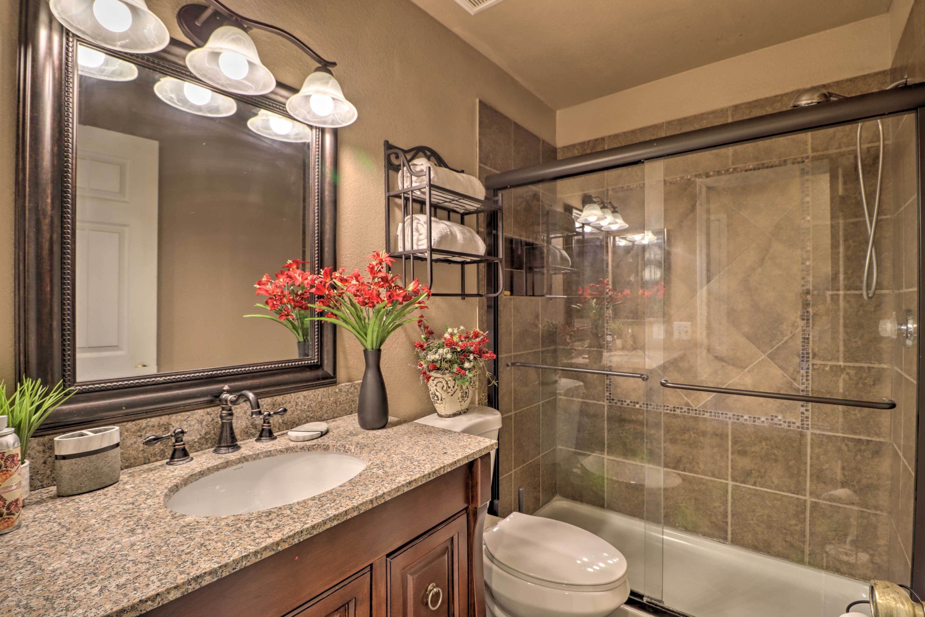 A bathroom with a granite countertop, a double sink, a large mirror, a shower enclosure, and a toilet.