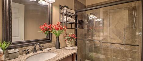 A bathroom with a granite countertop, a double sink, a large mirror, a shower enclosure, and a toilet.