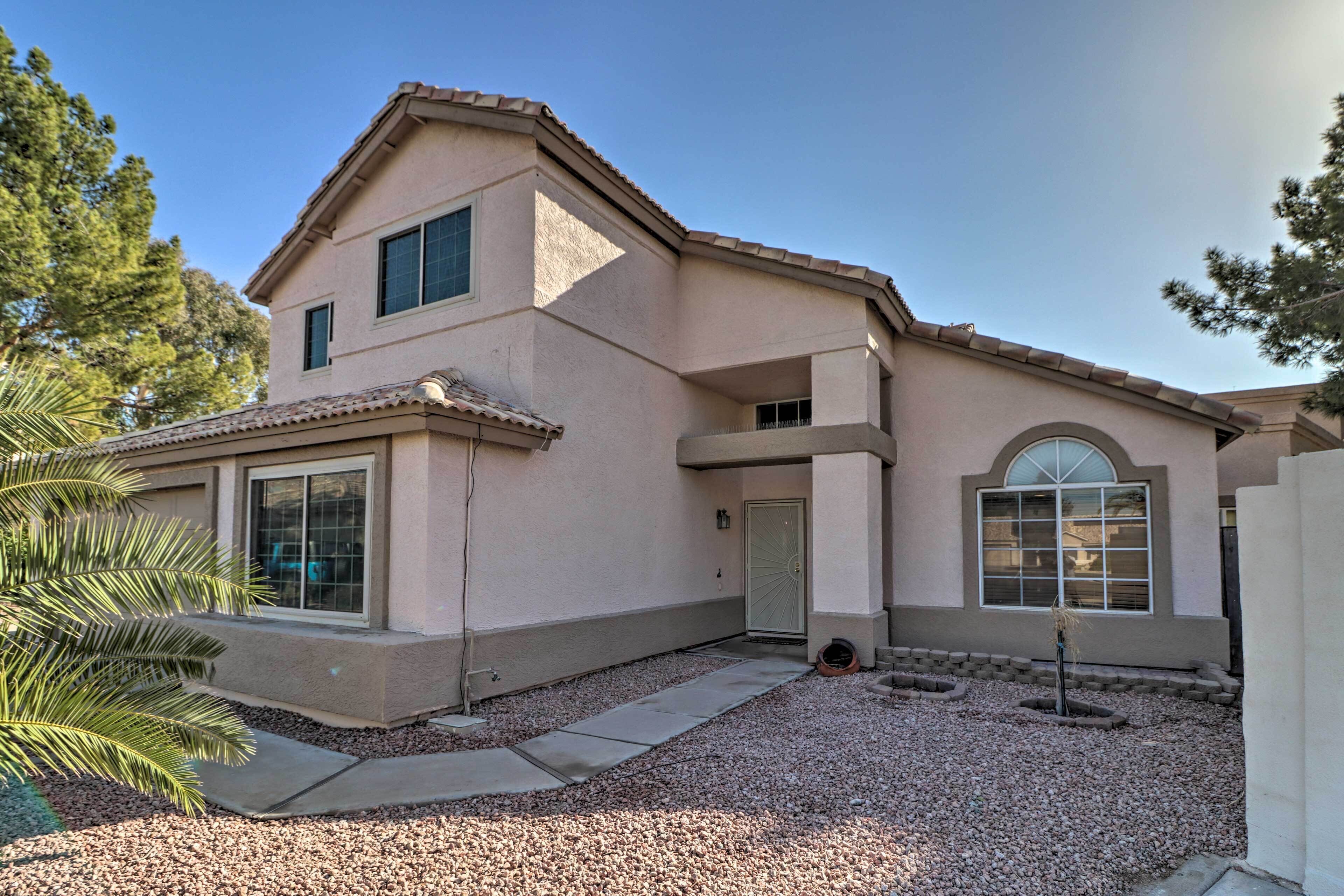 A two-story house with a beige exterior, a front porch, and a gravel driveway.