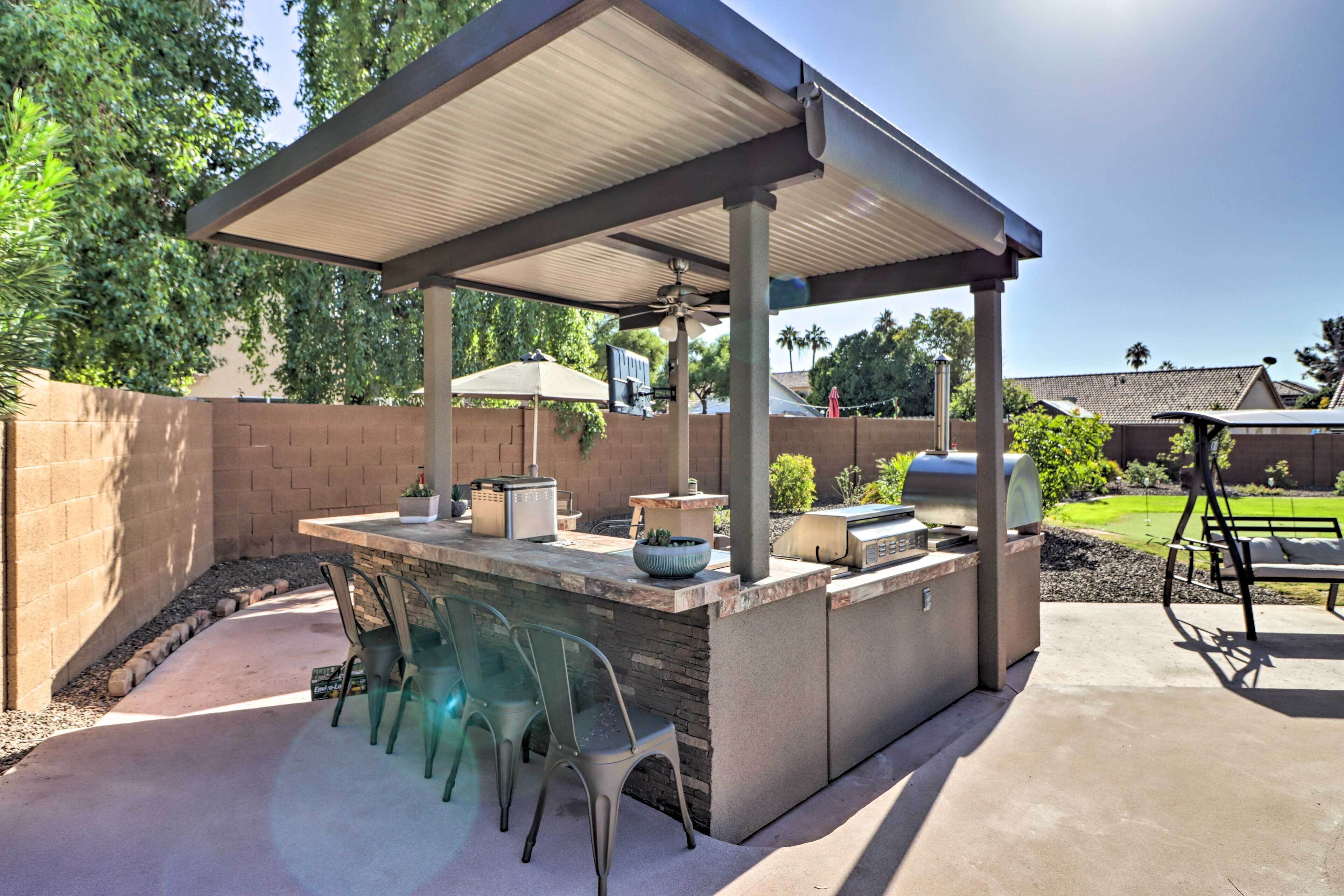 An outdoor patio with a covered grill station, seating area, and a view of the backyard.