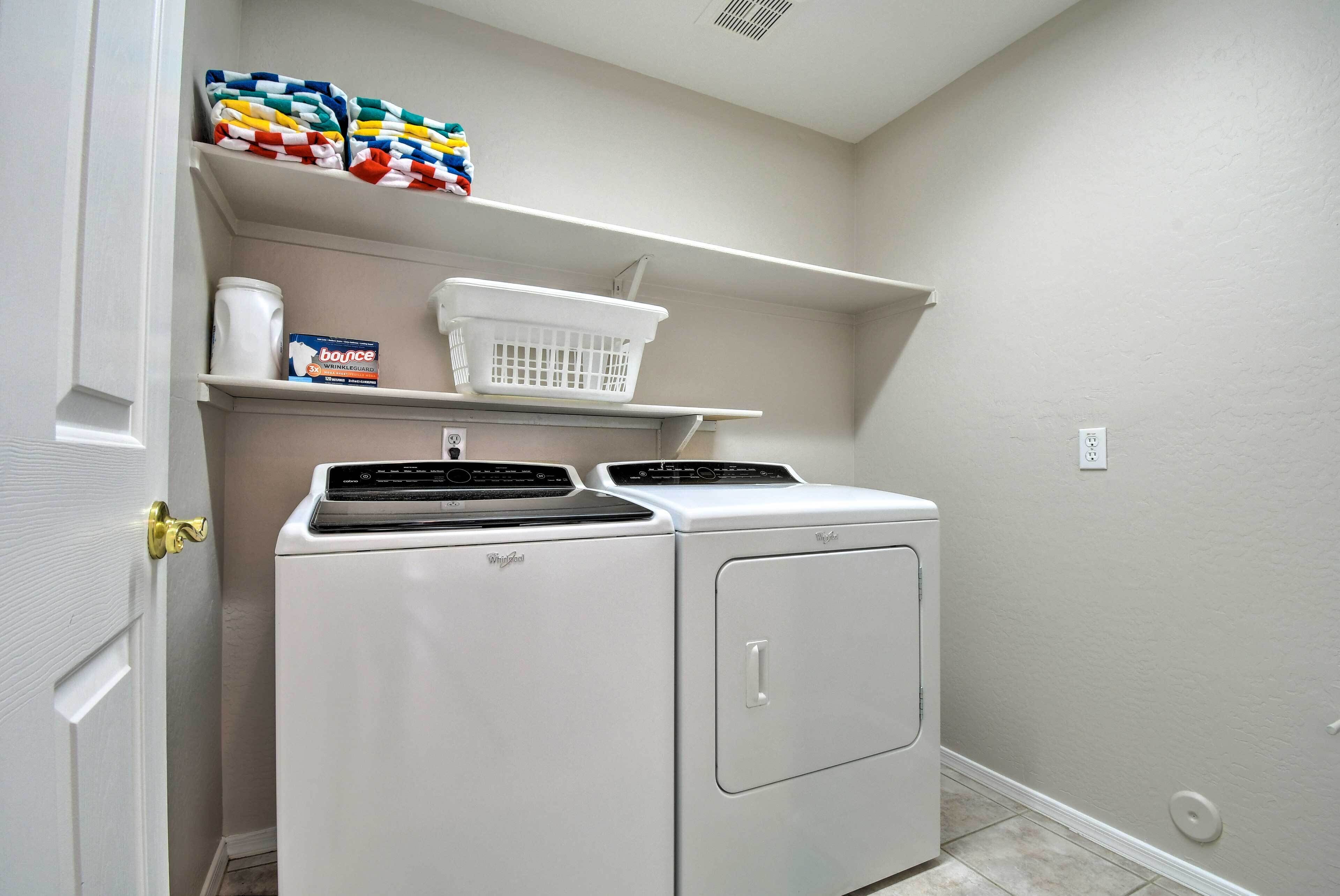 Een wasruimte met een voorlader wasmachine en droger, een wasmand en een doos wasmiddel op een plank.