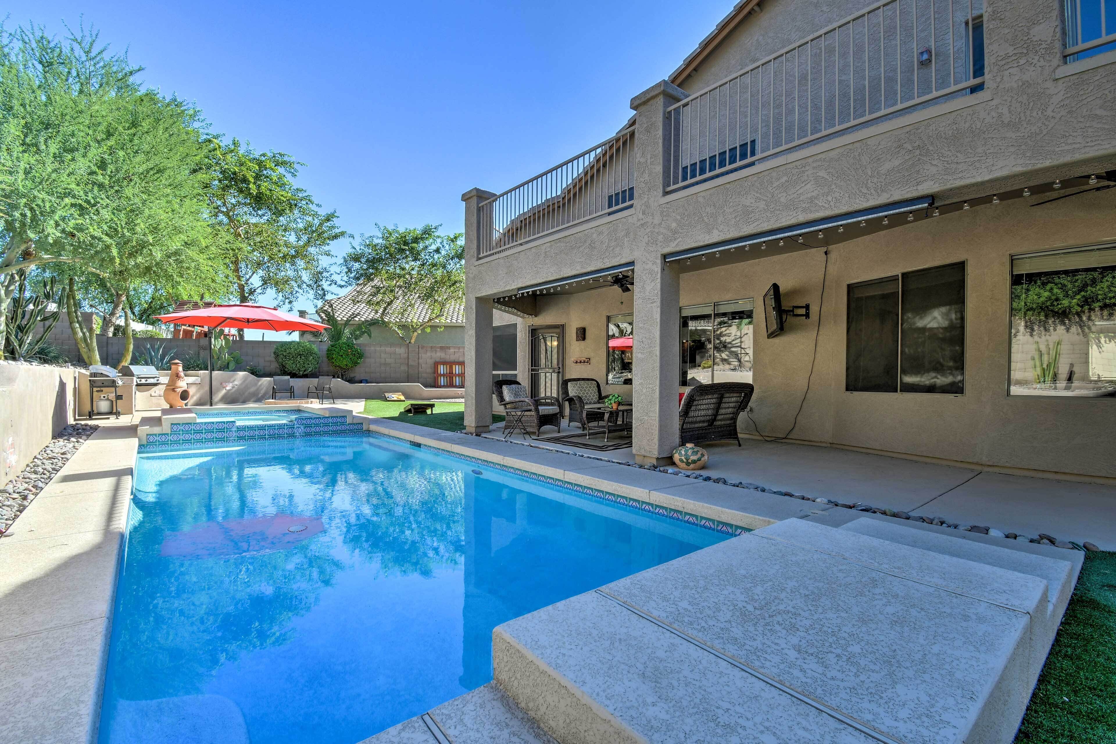 A backyard with a swimming pool, outdoor seating, and a two-story house.