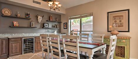 A dining area with a white table and chairs, a chandelier, and shelves with decorative items.