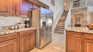 A kitchen with wooden cabinets, a stainless steel refrigerator, granite countertops, and a stone fireplace. - Hot Tub & Fire Pit: Mtn-view Mesa Home! (Mesa)