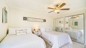 A hotel room with two beds, a ceiling fan, a mirror, and a wall with framed pictures and a sign.