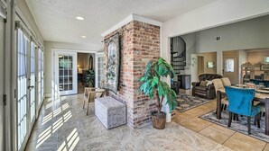 A spacious living area with a brick accent wall, a large potted plant, a dining table with chairs, and a fireplace.