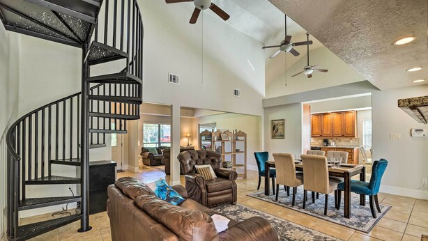 A spacious living area with a spiral staircase, leather furniture, a dining area with blue chairs, and a kitchen in the background.