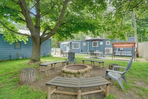 A backyard with a fire pit, wooden benches, and a covered seating area.