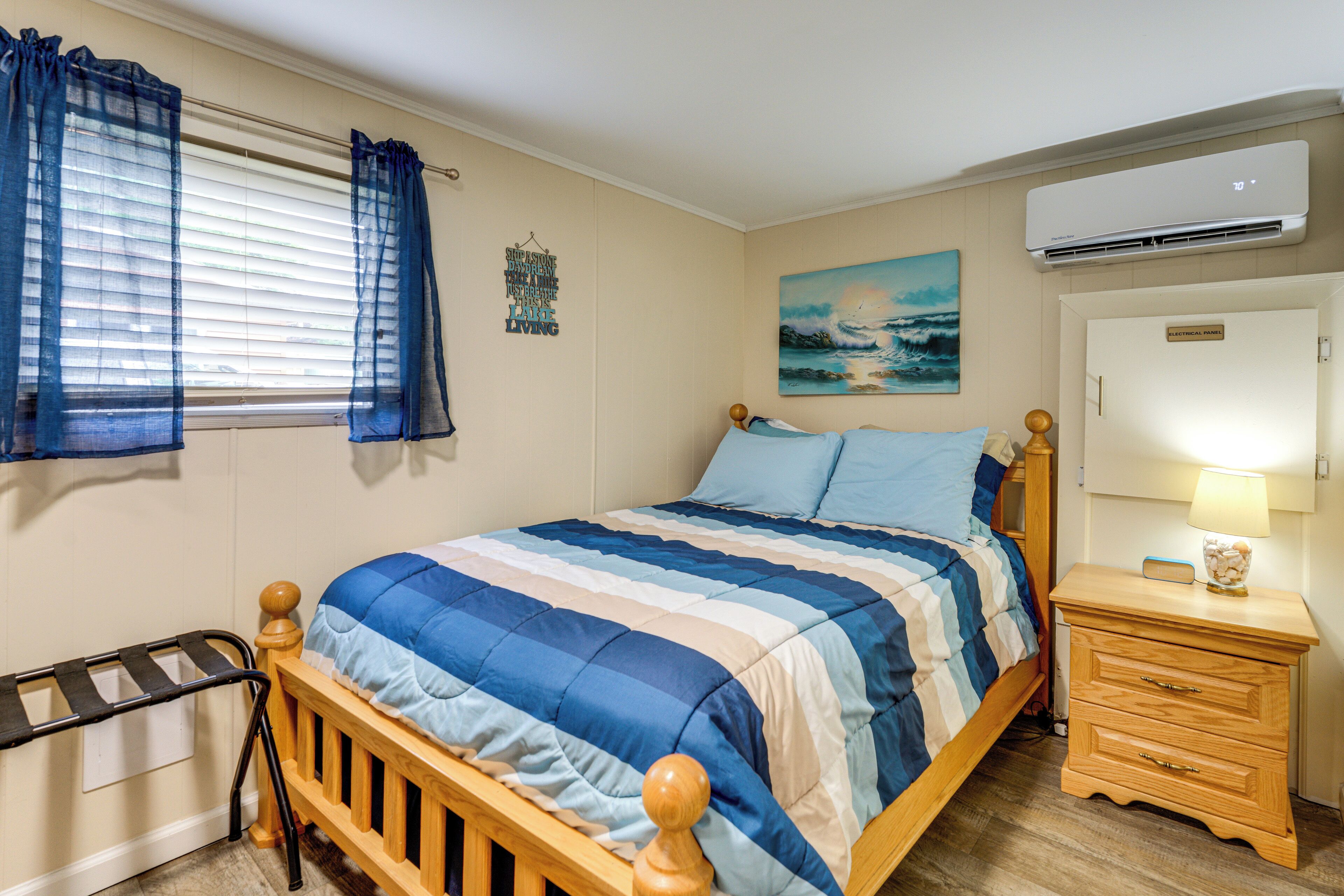 A bedroom with a bed, a nightstand, a mirror, a window with curtains, and an air conditioning unit.