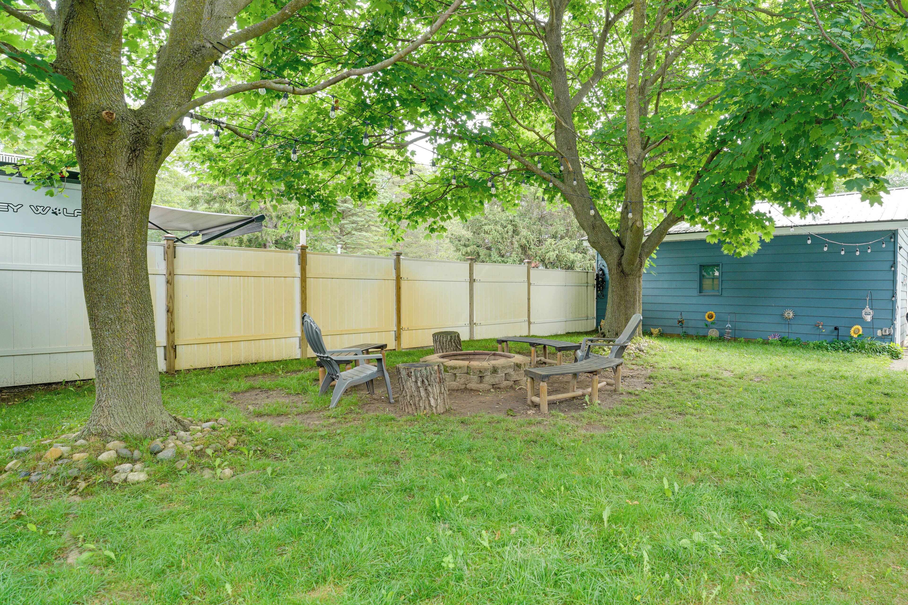 Un jardin avec un arbre, un banc en bois, un foyer et un camping-car blanc.