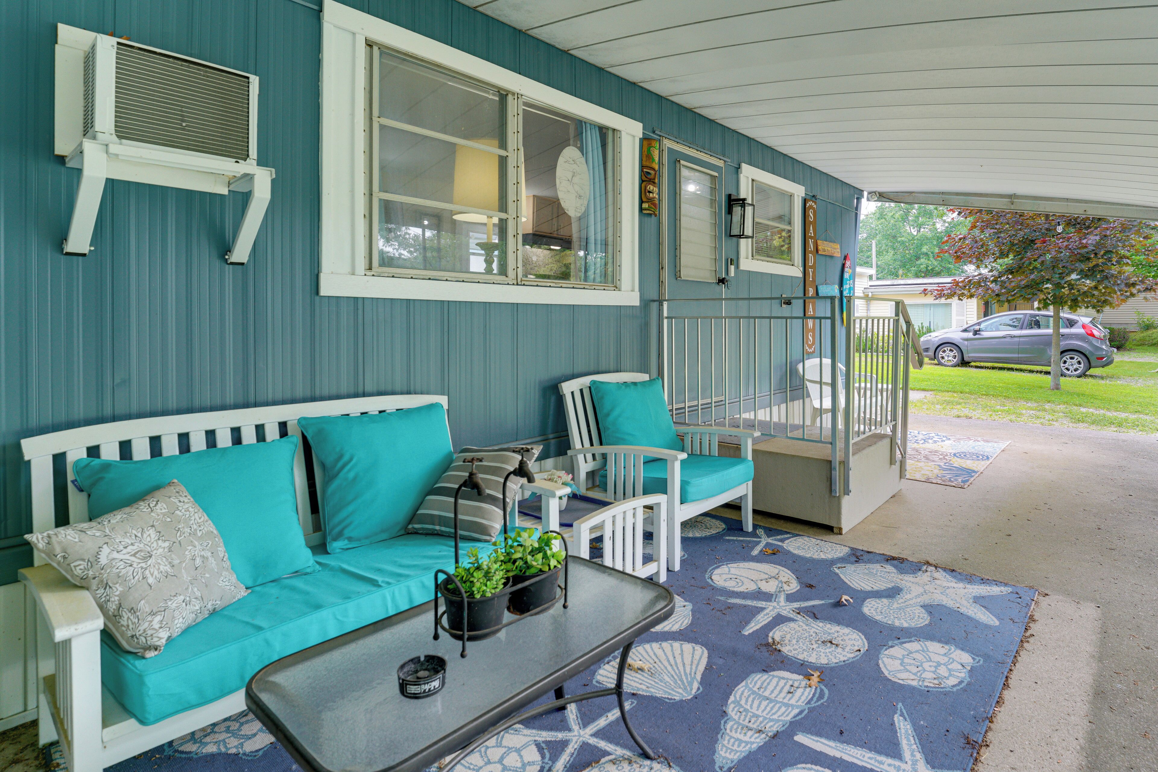 A covered porch with a blue and white color scheme, featuring a white bench, a white chair, a small table with a plant, and a starfish-patterned rug.