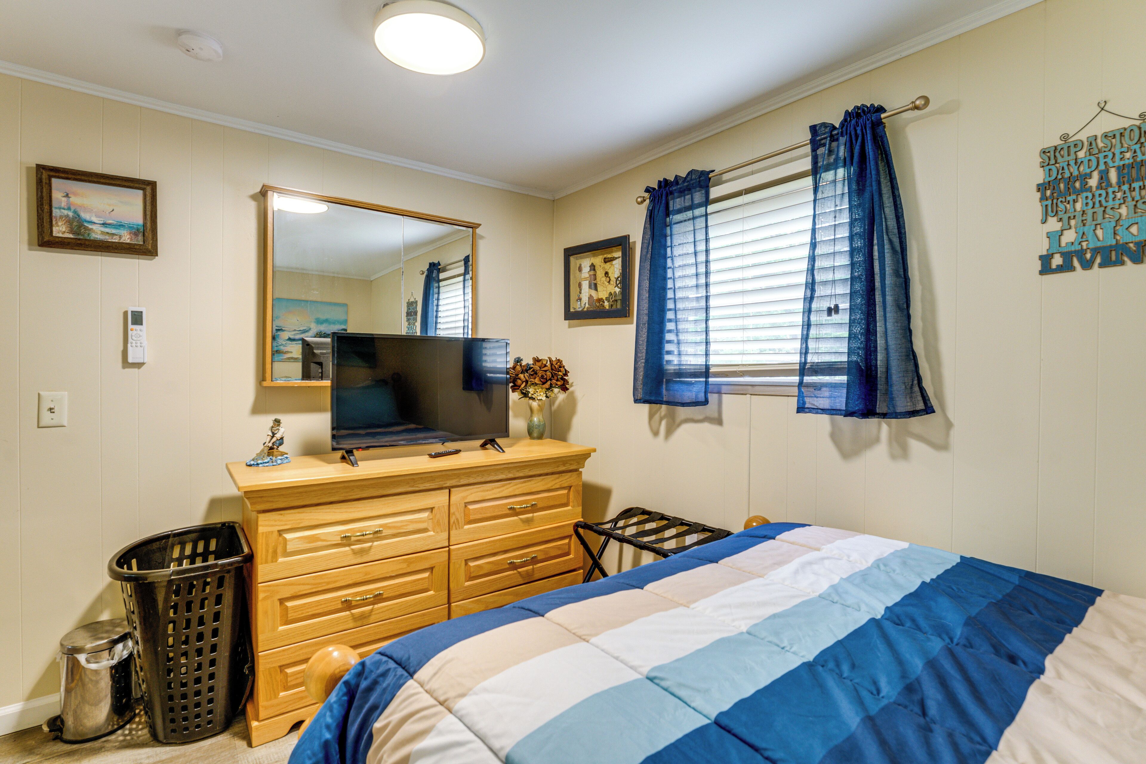 A bedroom with a bed, dresser, television, and a window with curtains.