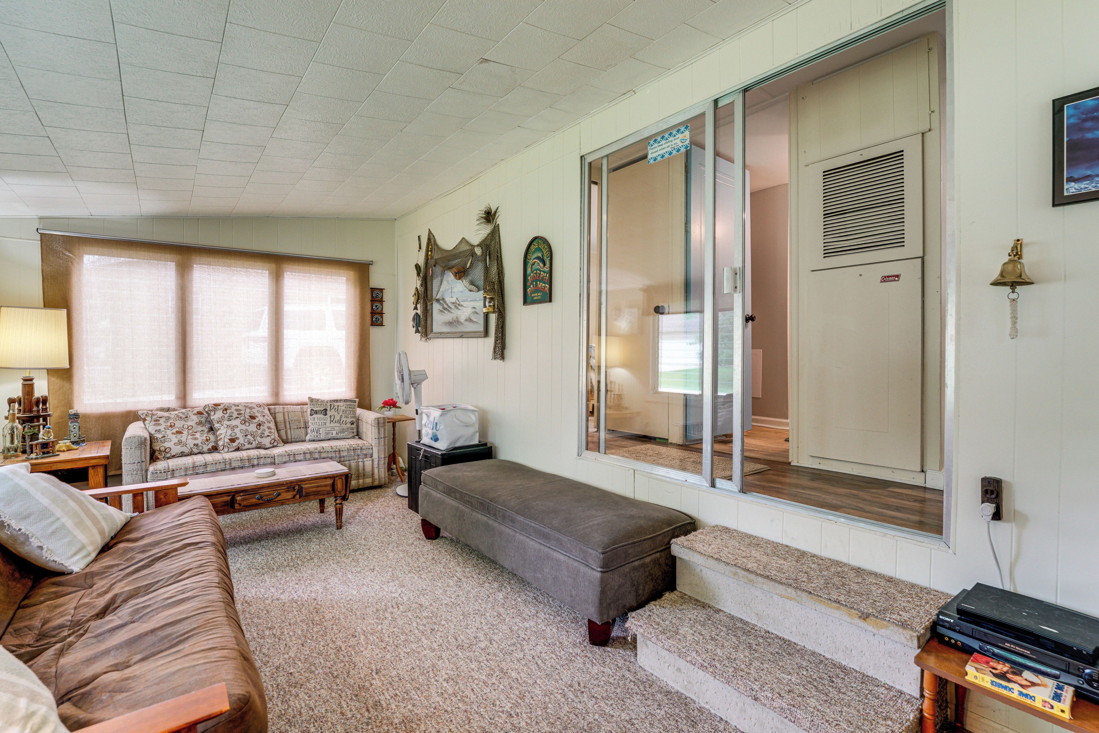 A living room with a sofa, bench, and a coffee table. There is a door with a mirror and a window with blinds.