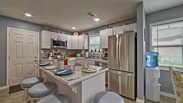 A modern kitchen with white cabinets, stainless steel appliances, a central island with stools, and a water dispenser.