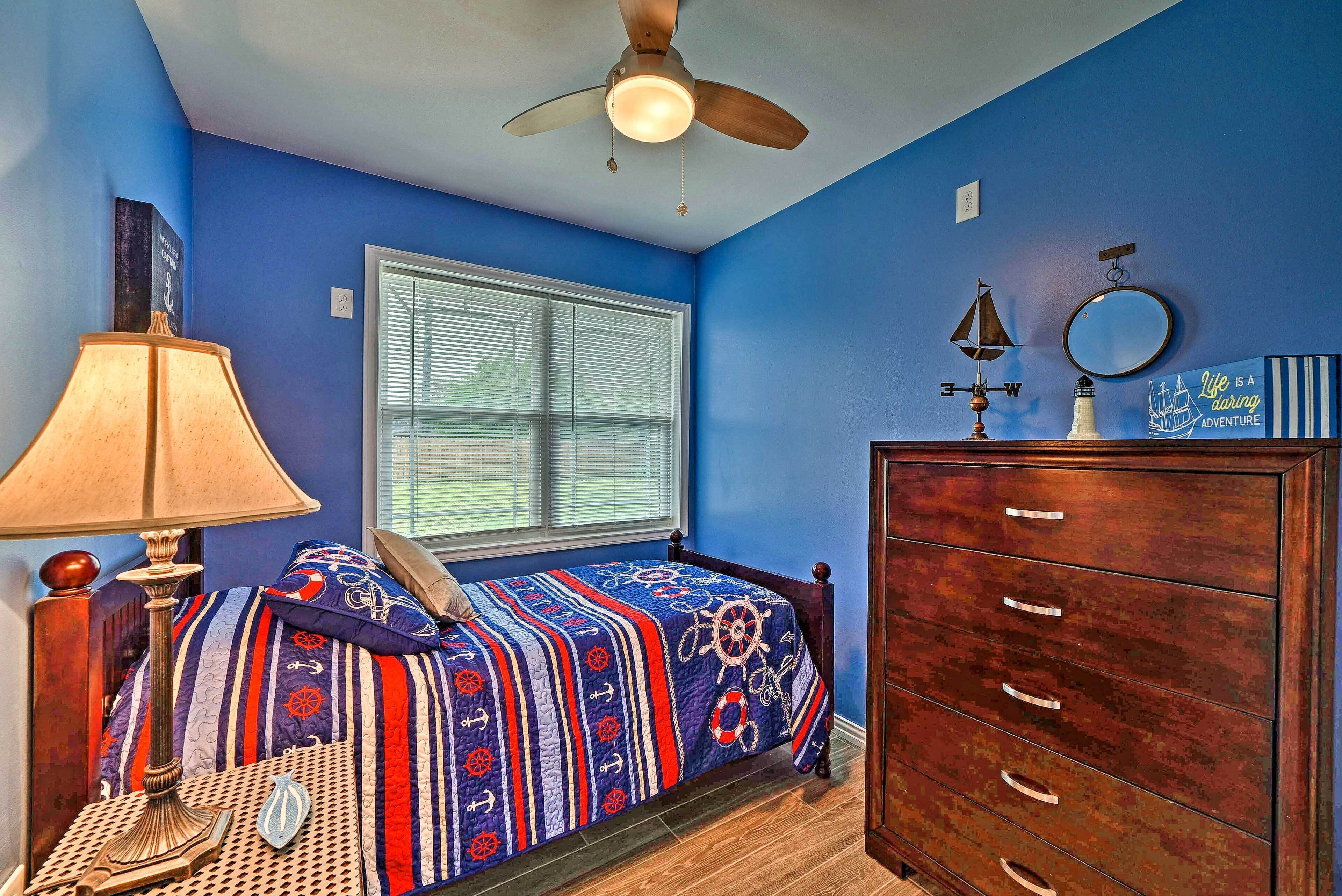 A bedroom with a bed, dresser, lamp, and a ceiling fan.