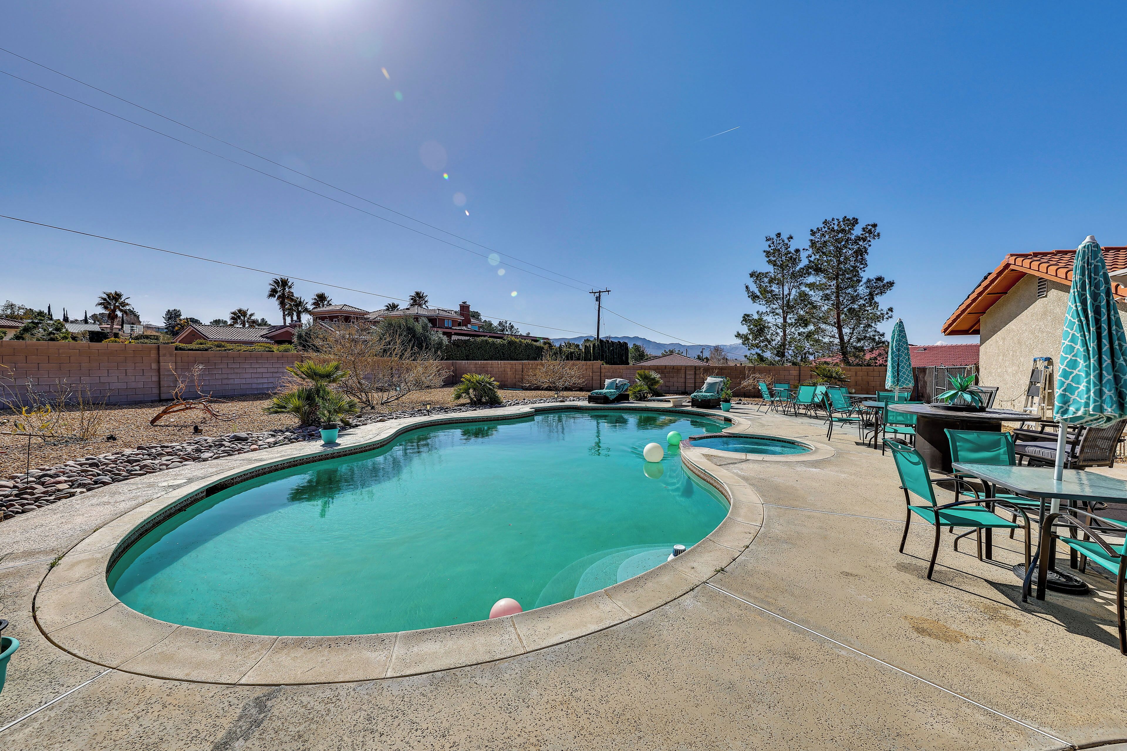 A swimming pool with a curved edge, surrounded by a patio area with green chairs and umbrellas.