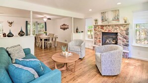 A living room with a fireplace, a dining area, and a seating area with patterned sofas.