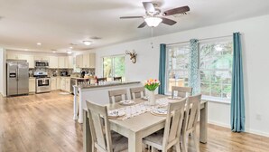 A modern kitchen with stainless steel appliances, a dining area with a wooden table and chairs, and a ceiling fan.