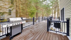 A wooden deck with a grill, a railing, and a building in the background.