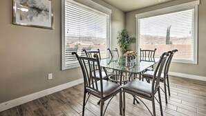 A dining area with a glass table surrounded by metal chairs, large windows with blinds, and a framed abstract painting on the wall. - Modern Vacation Rental Near Zion National Park! (La Verkin)