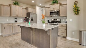 A modern kitchen with light wood cabinets, a granite island, stainless steel appliances, and decorative plants. - Modern Vacation Rental Near Zion National Park! (La Verkin)