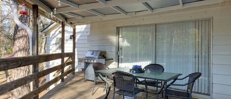 A covered patio with a table and chairs, a grill, and a string of lights.