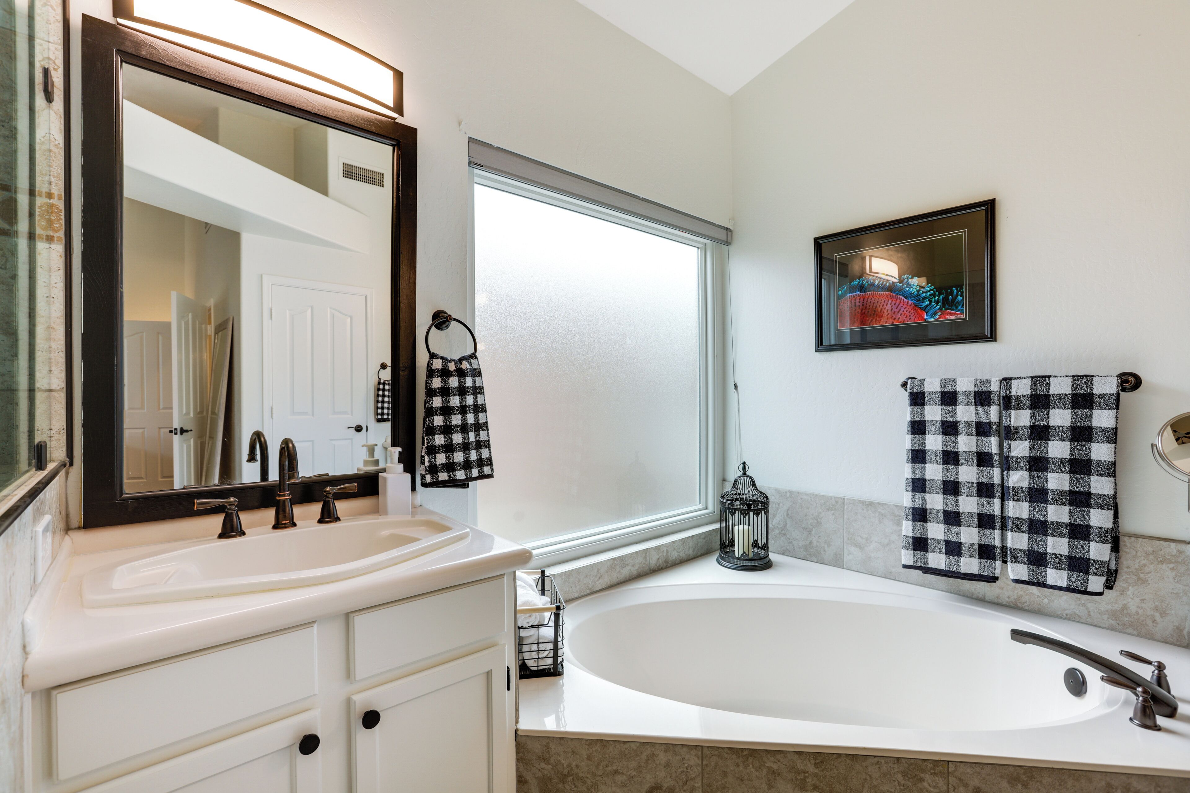 A bathroom with a white sink, a large mirror, a bathtub, and two checkered towels hanging on the wall.
