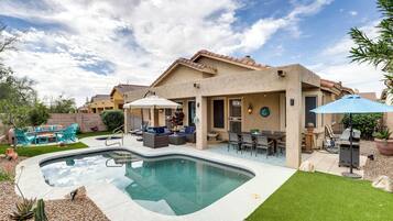 A backyard with a swimming pool, patio furniture, and a covered outdoor seating area.