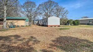 A mobile home with a green roof, a fenced yard, and leaf-covered ground. - Peaceful Supply House ~ 2 Mi to Holden Beach! (Supply)