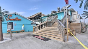 A blue building with a sign reading "Sandbar" and a wooden staircase leading to a deck.